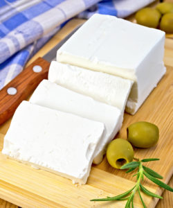 Feta cheese, knife, rosemary, olives, blue checkered napkin on the background of wooden boards