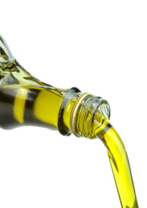 Pouring extra virgin olive oil from glass bottle on white background. 