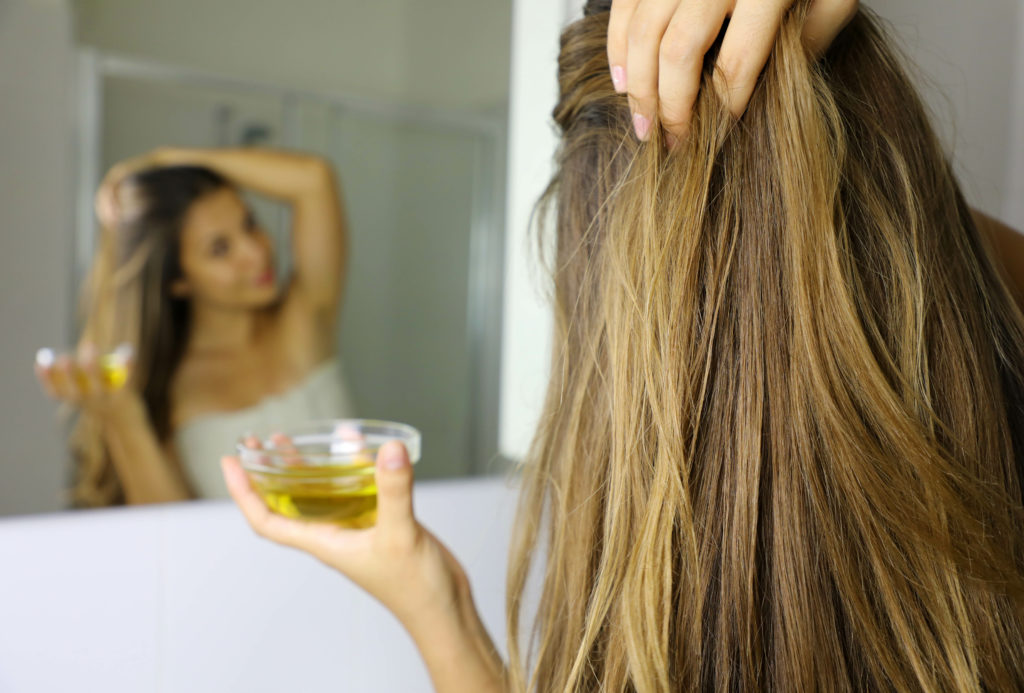 Young woman applying olive oil mask on hair in front of a mirror