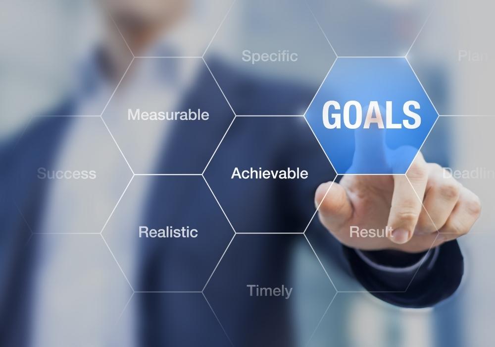 Man pointing to graphic with the word goals and descriptions like specific, measurable, achievable, realistic, and timely.